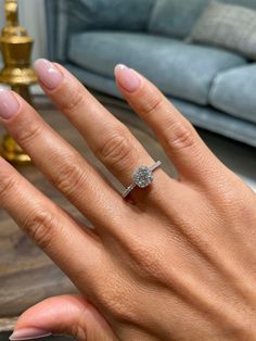 a woman's hand with a diamond ring on top of her finger, in front of a couch