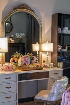 a dressing table with flowers on it and a mirror in the back ground, next to a chair