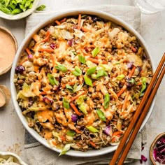 a bowl filled with rice and vegetables next to chopsticks on a table top