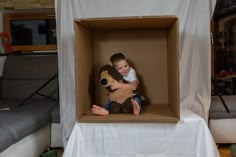 a little boy sitting in a cardboard box holding a teddy bear