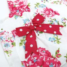 a red bow tied on top of a white shirt with pink flowers and polka dots