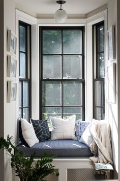 a window seat with pillows on it in front of a potted plant and other items