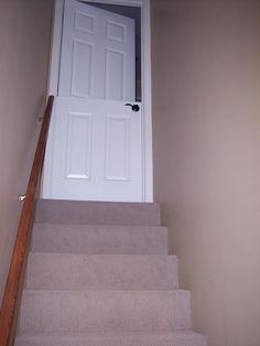 stairs leading up to an open door in a room with beige walls and carpeted flooring