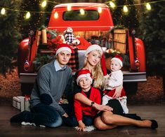 a family poses in front of a red truck with christmas lights on the tree and presents