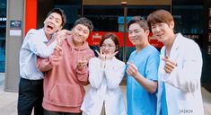 four people standing in front of a building giving the peace sign with their hands and fingers