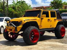 a yellow jeep with red rims parked in a parking lot