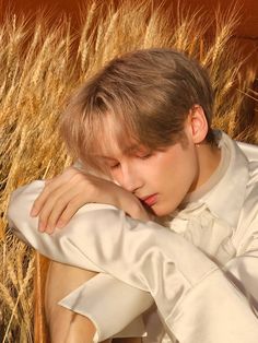 a young man sitting in front of some tall grass