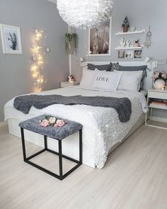 a white and gray bedroom with lights on the wall above the bed is decorated with pink flowers