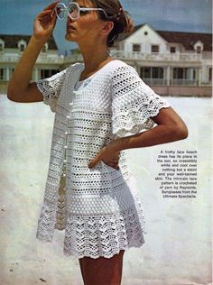 a woman in white crocheted dress standing on the beach with her hand under her eyeglasses