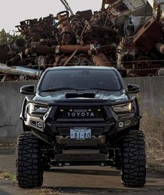 a black toyota truck parked in front of a pile of scrap metal items on the side of a road