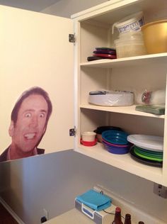 a kitchen with an open cupboard filled with plates and bowls next to a painting of a man's face on the wall