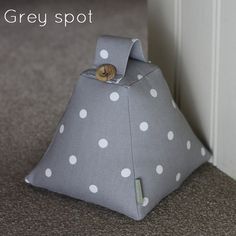 a grey spot bag sitting on the floor next to a white door with a wooden button in it