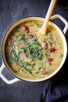 a pot filled with soup sitting on top of a wooden table next to a spoon