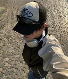 a young boy wearing headphones and a baseball cap is standing on a cobblestone street