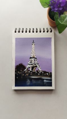 a painting of the eiffel tower on a notepad next to a potted plant