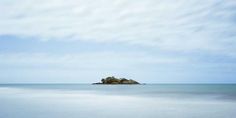 an island in the middle of the ocean with blue sky and white clouds above it