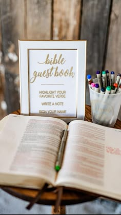 an open bible sitting on top of a wooden table next to a cup filled with crayons