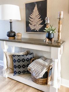 a white table topped with pillows and a lamp next to a painting on the wall