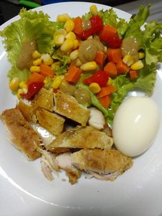 a white plate topped with chicken, lettuce and corn next to an egg