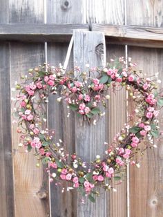 a heart shaped wreath with pink flowers hanging from the side of a wooden fence,