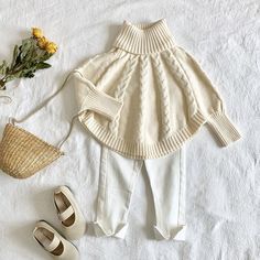 a white sweater and pants are on a bed next to shoes, a straw bag and flowers