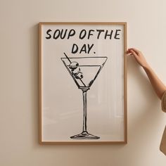 a woman standing next to a poster that says soup of the day with a martini in it