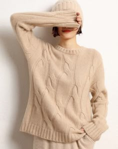 a woman wearing a sweater and pants with her hands on her head, leaning against a wall