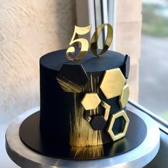 a black and gold birthday cake with five golden numbers on it's top, sitting in front of a window