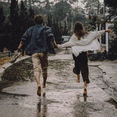 two people are walking down the street in the rain holding hands and one is carrying an umbrella