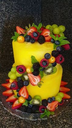 a three tiered cake decorated with fresh fruit on top of a granite countertop