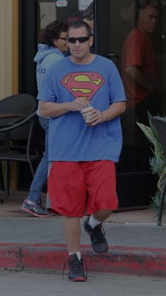 a man in a superman t - shirt and red shorts is walking down the street