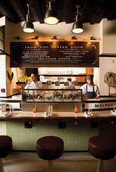 two men working behind the counter at a restaurant with stools in front of them