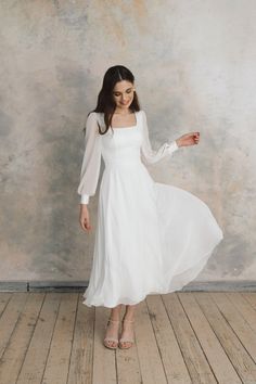 a woman in a white dress is standing on a wooden floor and posing for the camera