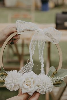 a person holding a white flower in front of a wooden hoop with ribbons on it