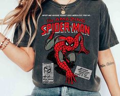 a woman wearing a spiderman t - shirt with her hands in her pockets and looking at the camera