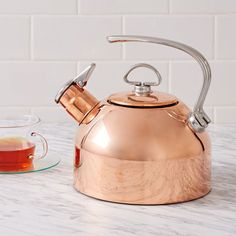 a copper tea kettle sitting on top of a marble counter next to a glass cup