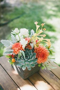 a wooden table topped with a vase filled with flowers and succulents on top of it