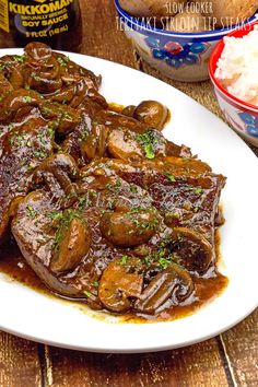 a white plate topped with meat and mushrooms covered in gravy next to rice