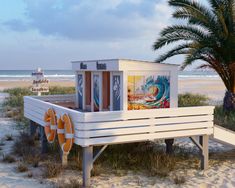 a white bench sitting on top of a sandy beach next to the ocean and palm trees