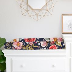 a white dresser with flowers on it next to a mirror and framed photograph in the corner