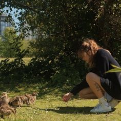 a woman kneeling down in the grass with ducks around her and one duckling on the ground