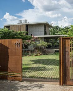 an open gate leading to a house in the middle of a yard with trees and bushes