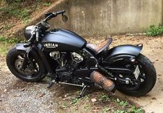 a black motorcycle parked on the side of a road next to a cement wall and grass