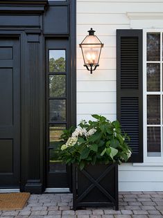 a black door with shutters and a planter on the front porch next to it