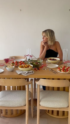 a woman sitting at a wooden table with plates and bowls of food in front of her