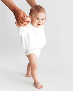 a man holding the hand of a baby who is wearing a white sweater and diaper