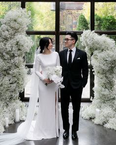 a man and woman standing next to each other in front of white flowers on display