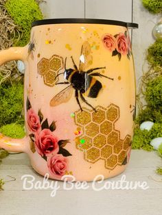 a coffee mug with a bee and flowers painted on the inside is sitting in front of some moss