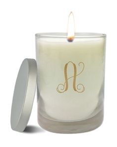 a white candle with a gold monogrammed letter on the front and bottom, sitting next to a silver container