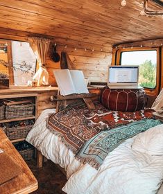 a bed with a laptop on top of it next to a desk and window in a cabin